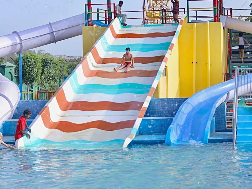 A kid coming down from a slide to the pool.